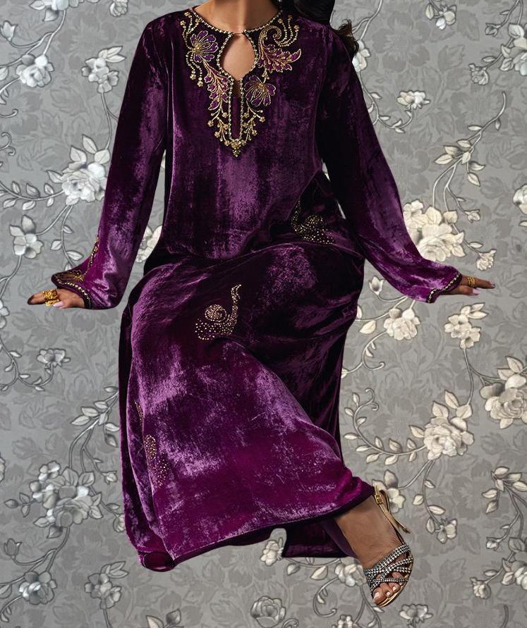 A woman wearing a long purple velvet dress with gold embroidery and a floral pattern on the background.