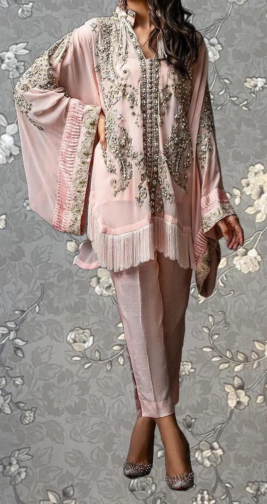 A woman wearing a pink and white dress with intricate embroidery and frills, standing against a gray floral background.