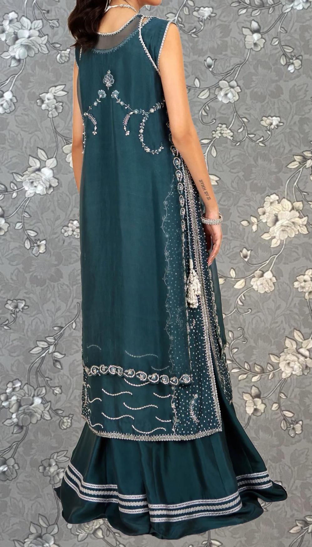 A woman wearing a long, sleeveless green dress with intricate embroidery and a matching skirt.