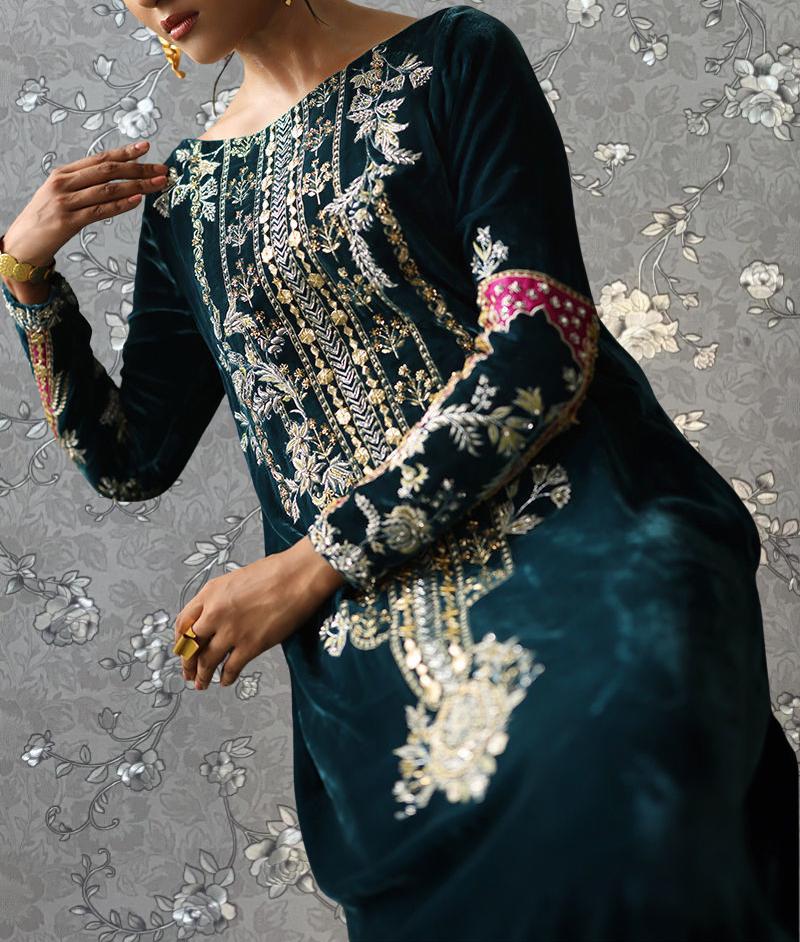 A woman wearing a long, dark green dress with intricate gold embroidery and floral patterns.