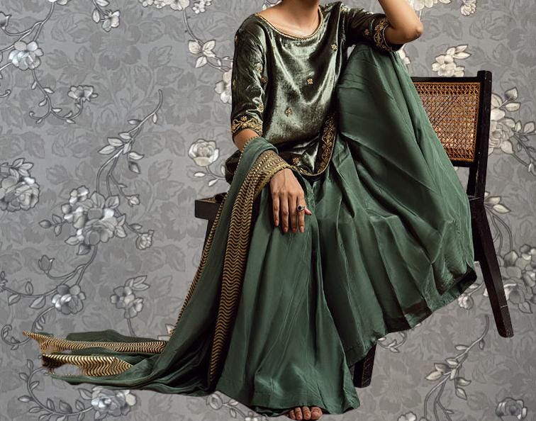A woman wearing a green and gold dress is sitting on a chair against a gray floral background.