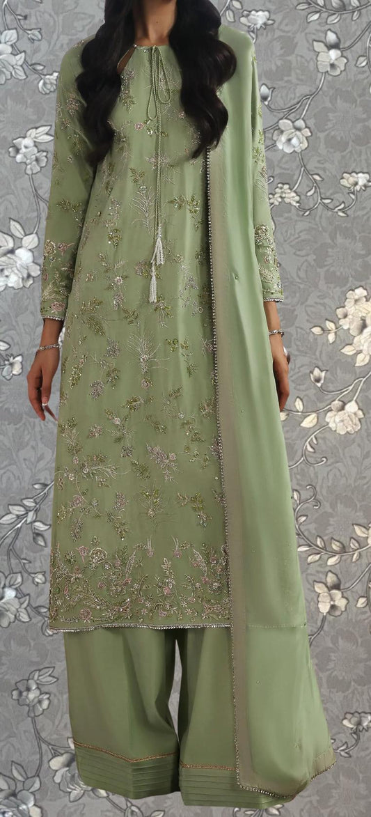 A woman wearing a green dress with intricate embroidery and a matching green shawl.