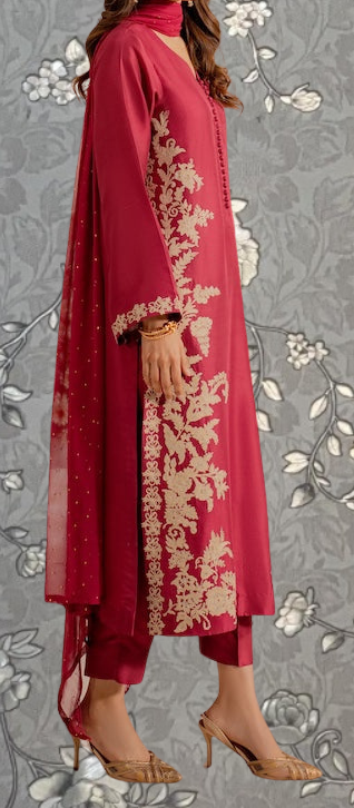 A woman wearing a red and gold dress with intricate embroidery stands against a gray floral background.