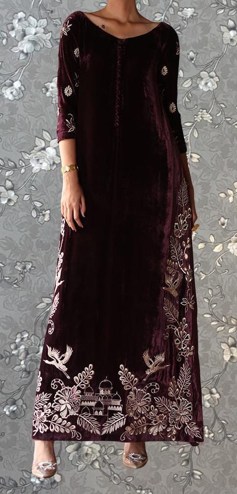 A woman wearing a long, burgundy velvet dress with intricate embroidered designs on the sleeves and hem.