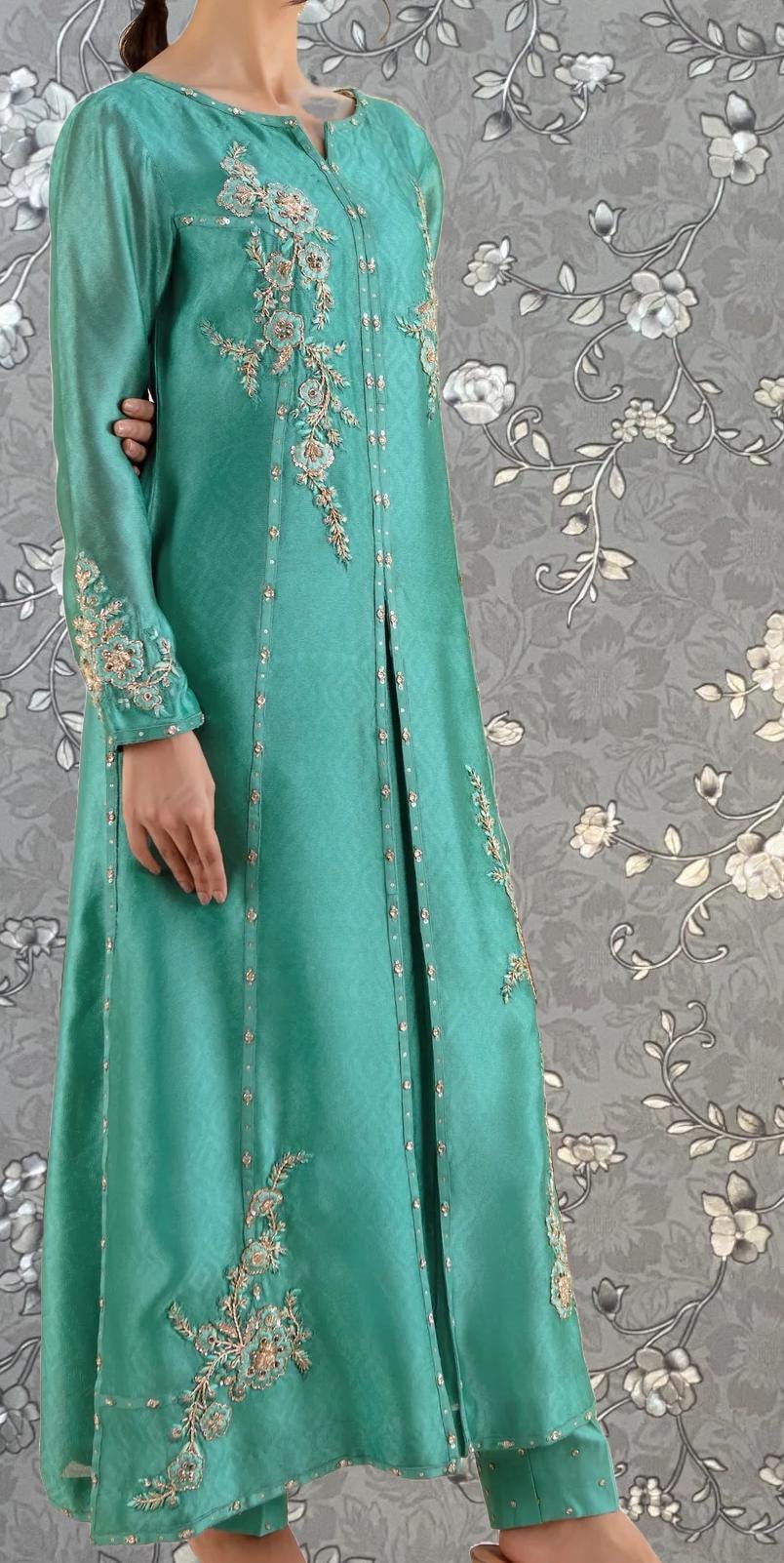 A mannequin wearing a long, turquoise-colored dress with intricate embroidered designs on the sleeves and hem.