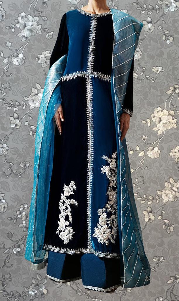 A woman wearing a long blue dress with white floral embroidery and a matching blue shawl.