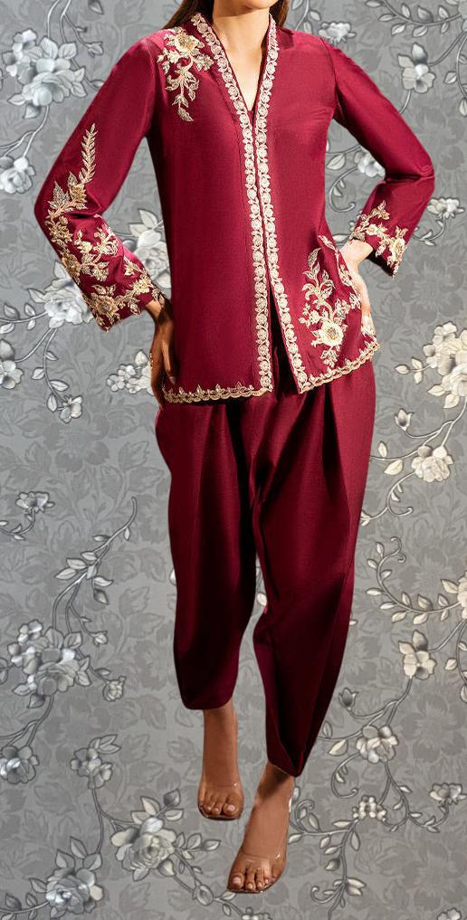 A woman wearing a red and gold patterned outfit stands against a gray floral background.