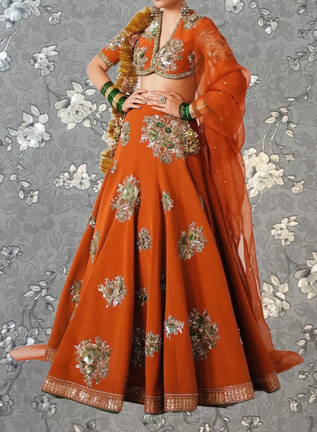 A woman wearing an ornate, brightly colored orange and gold dress with intricate embroidery and a matching orange shawl.