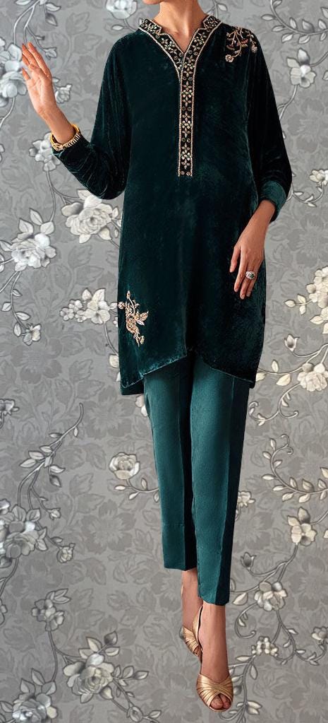 A person wearing a green velvet dress with gold embroidery and gold heels is standing against a gray floral background.