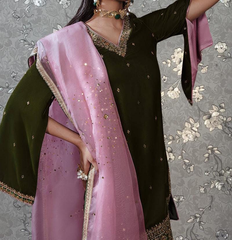 A woman wearing a dark green dress with a pink shawl and gold accents, posing against a gray floral background.