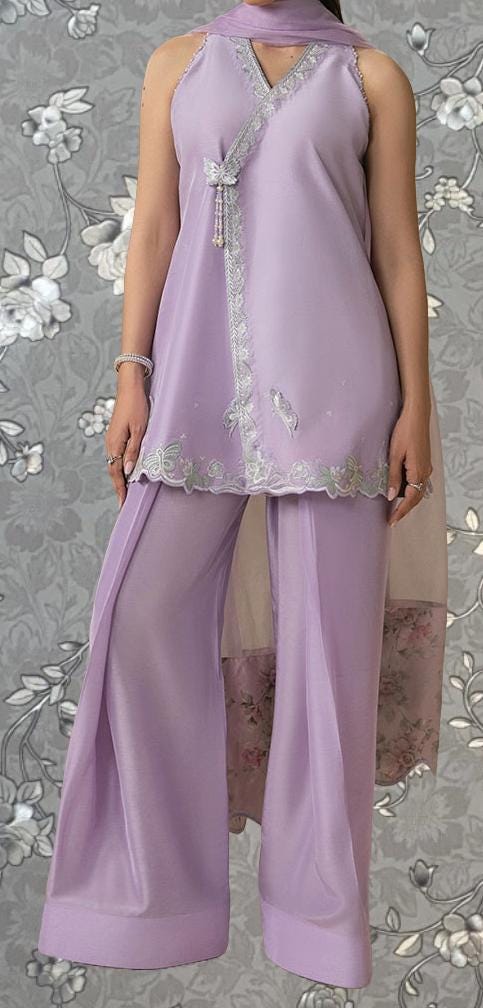 A woman wearing a purple dress with a floral pattern and a matching purple skirt, standing against a gray floral background.
