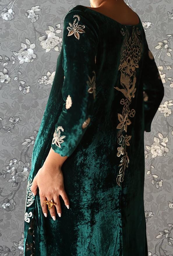 A person wearing a long, green velvet dress with intricate embroidered designs on the back.