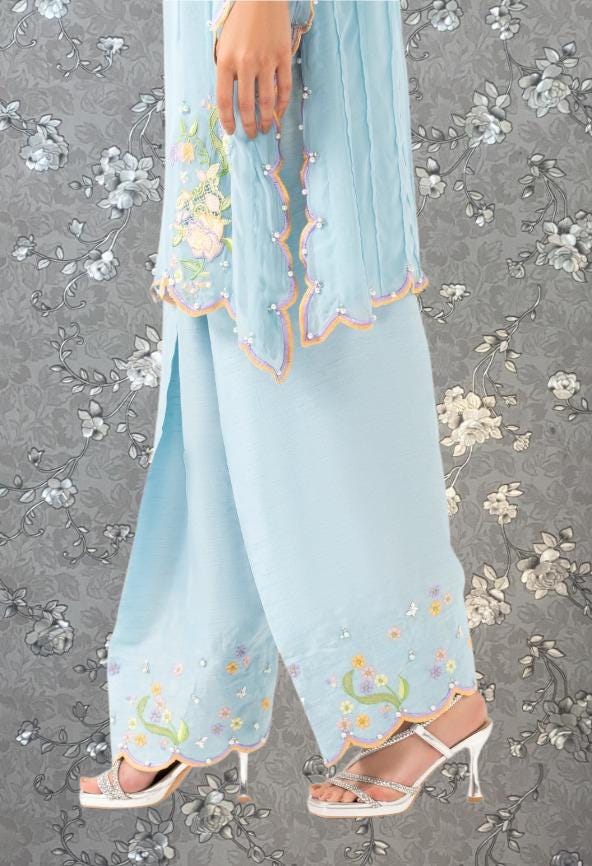 A person wearing a light blue dress with floral embroidery and high-heeled sandals, standing against a gray floral background.
