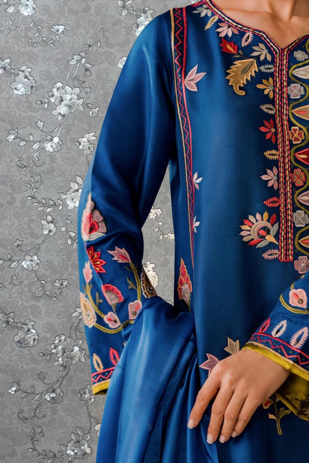 A close-up view of a person wearing a blue dress with intricate embroidered patterns in shades of red, gold, and white.