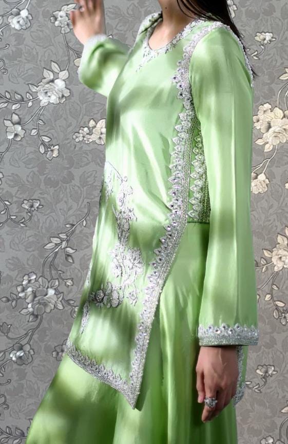 A woman wearing a long, green dress with intricate embroidery and a matching green skirt.