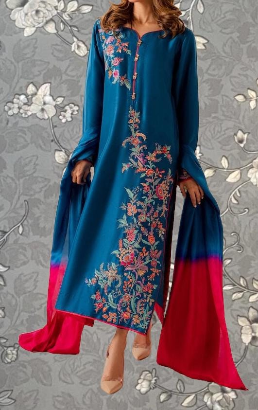 A woman wearing a blue dress with floral embroidery and a red shawl.