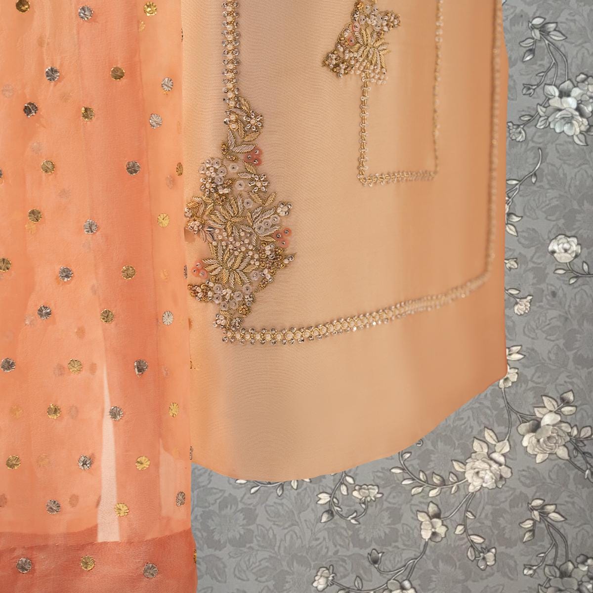 a close-up view of a fabric with intricate embroidery and a floral pattern. The fabric appears to be a light peach color, with a gold and white floral design. The background is a gray floral pattern.