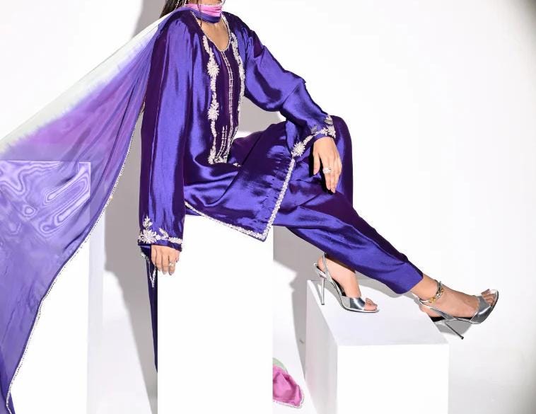 A person wearing a purple outfit with a long purple scarf is sitting on a white pedestal.