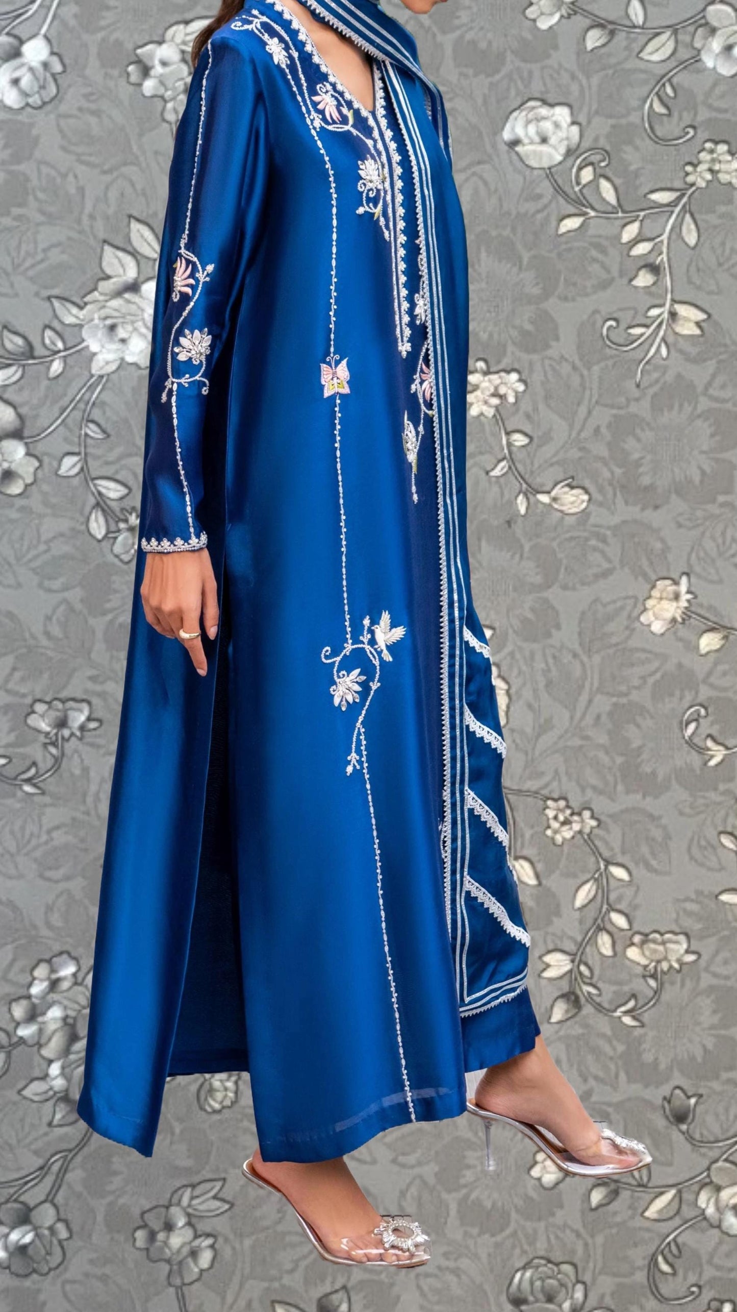 A person wearing a long, blue dress with intricate embroidered designs on the sleeves and hem.