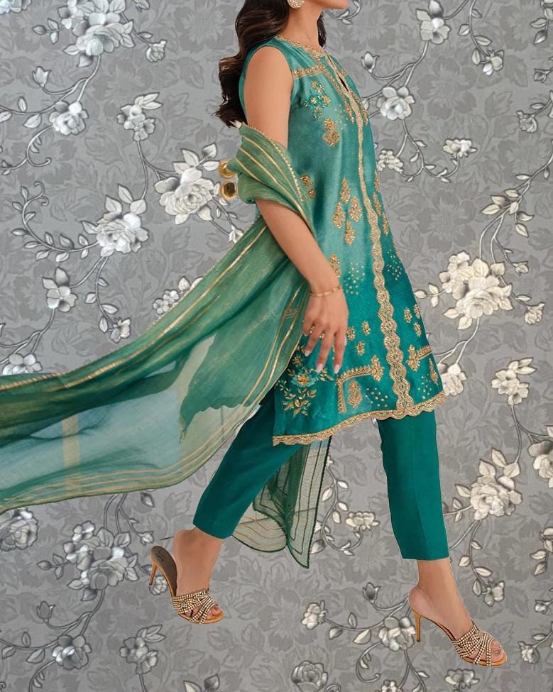 A woman wearing a green and gold dress with a matching green shawl, standing against a gray floral background.