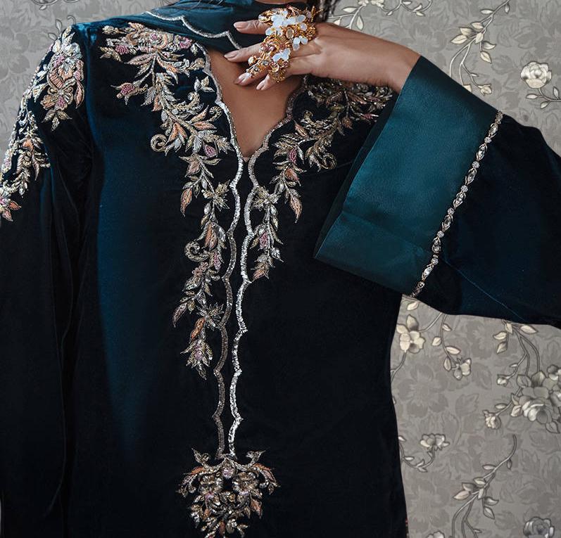 A close-up of a person wearing a dark blue dress with intricate embroidered patterns and jewelry.