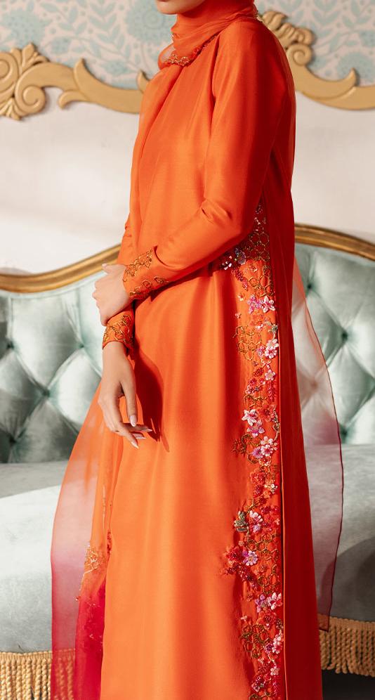 A person wearing an orange dress with floral embroidery stands in front of a blue couch.