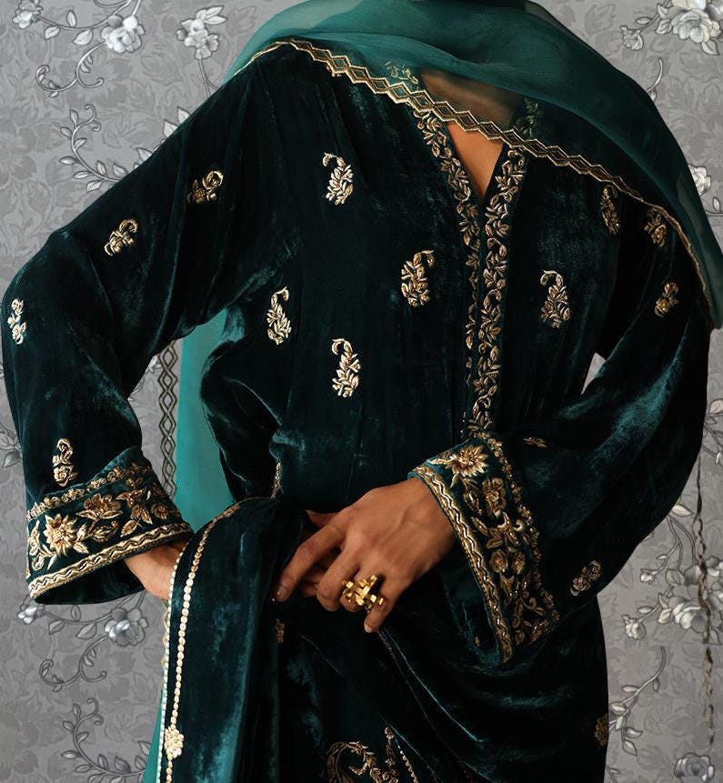 A close-up of a person wearing a dark green velvet dress with gold embroidery, including a matching green shawl.