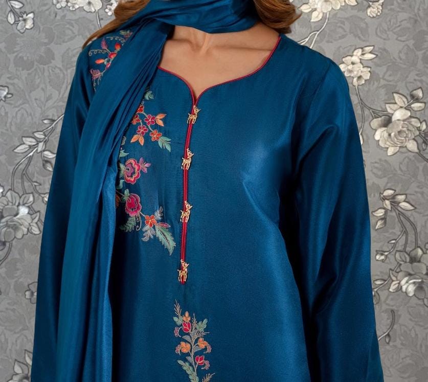 A close-up of a woman wearing a blue dress with intricate floral embroidery on the front.