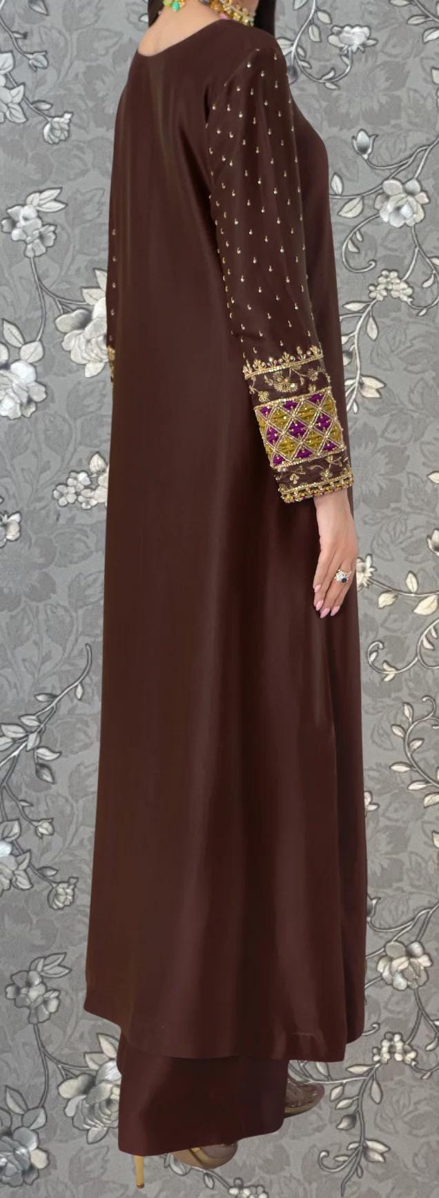 a woman wearing a long brown dress with gold embroidery on the sleeves.