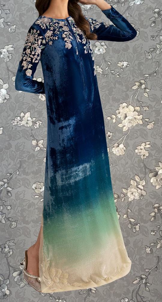 A woman wearing a long, blue velvet dress with intricate floral embroidery on the sleeves and hem.