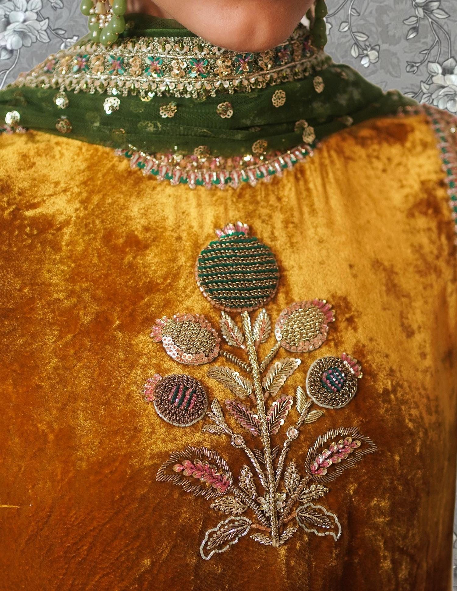 a close-up view of a gold velvet dress with intricate embroidered designs, including a large floral motif.
