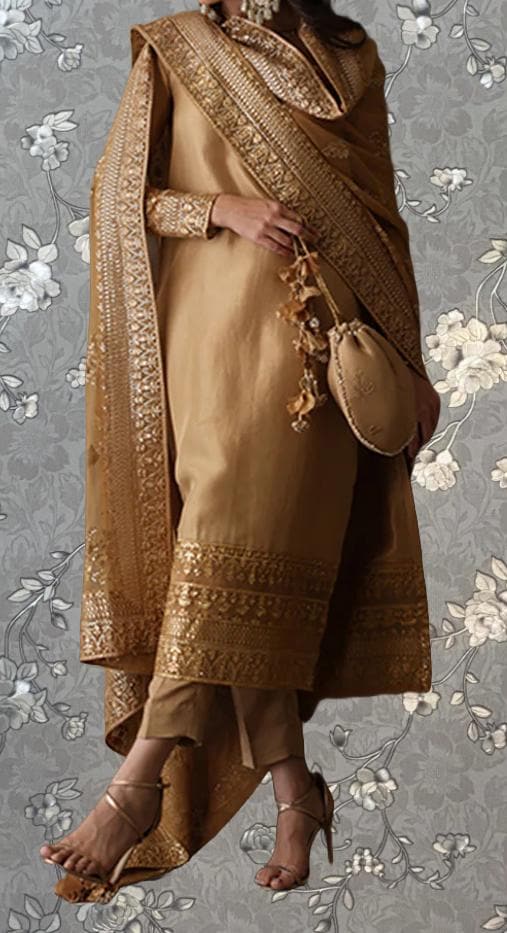 A woman wearing a gold and beige dress with a matching gold and beige shawl, standing against a gray floral background.