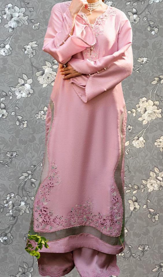 A woman wearing a long pink dress with floral embroidery stands against a gray floral background.