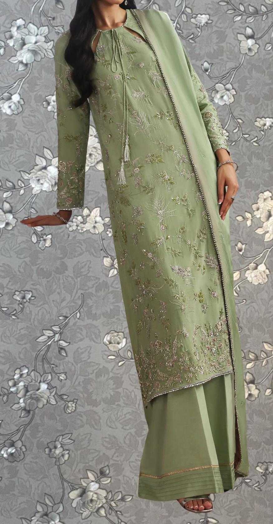 A woman wearing a long, green dress with intricate embroidery and floral patterns.