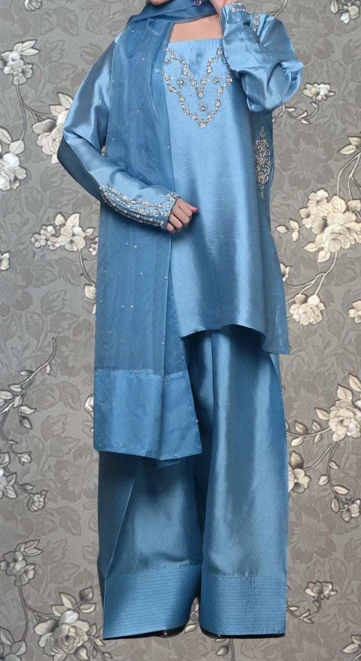 A person wearing a blue dress with intricate embroidery and a matching blue scarf.