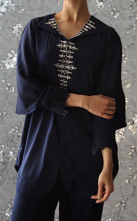 A person wearing a navy blue dress with a floral pattern and a high collar, posing against a gray floral background.