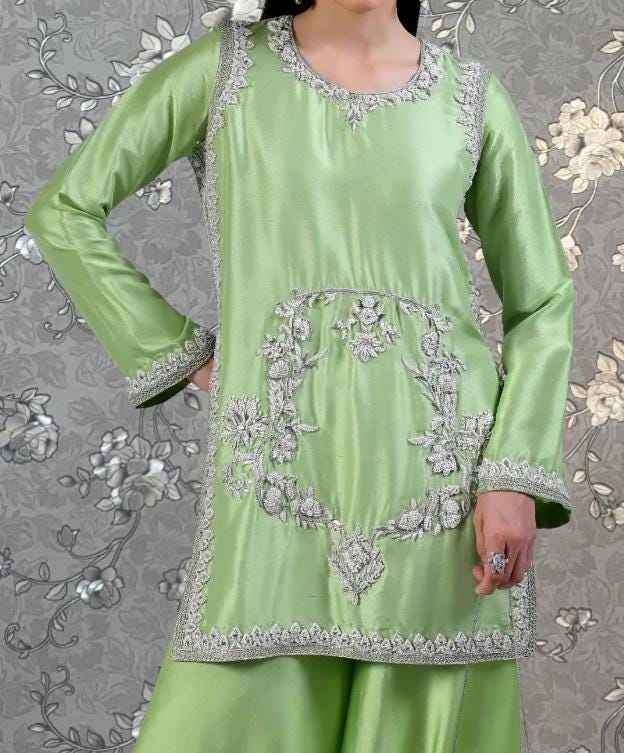 A woman wearing a green dress with intricate embroidery and floral patterns.