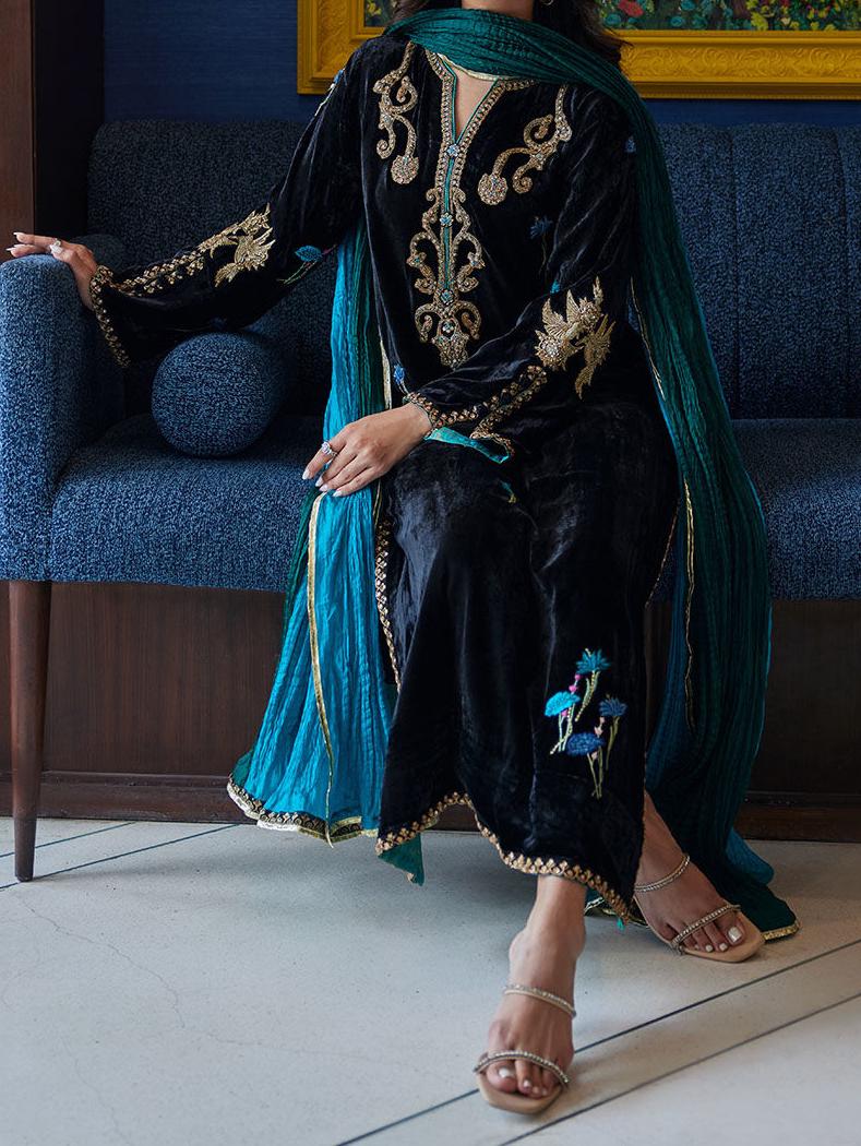 A woman wearing a black and blue dress with gold embroidery is sitting on a blue couch.
