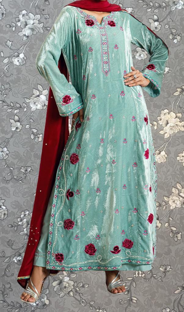 A woman wearing a long, light blue dress with red floral embroidery and a matching red shawl.