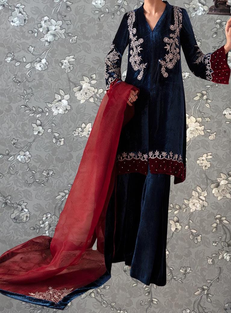 A person wearing a blue velvet dress with red embroidered details and a matching red shawl.