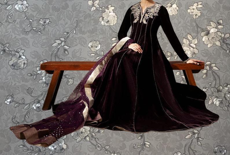 A woman wearing a long, dark purple dress with a white floral pattern sits on a wooden bench against a gray floral background.