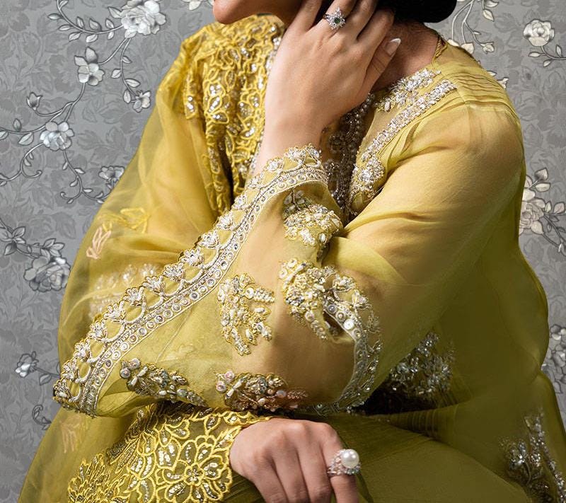 A close-up of a person wearing a yellow and gold dress with intricate embroidery and jewelry, including a ring on their finger.