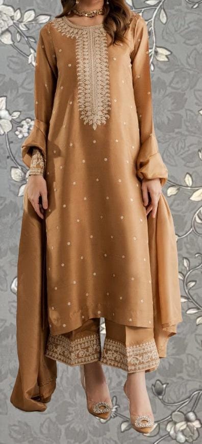 A woman wearing a gold-colored dress with a floral pattern, standing against a gray floral background.