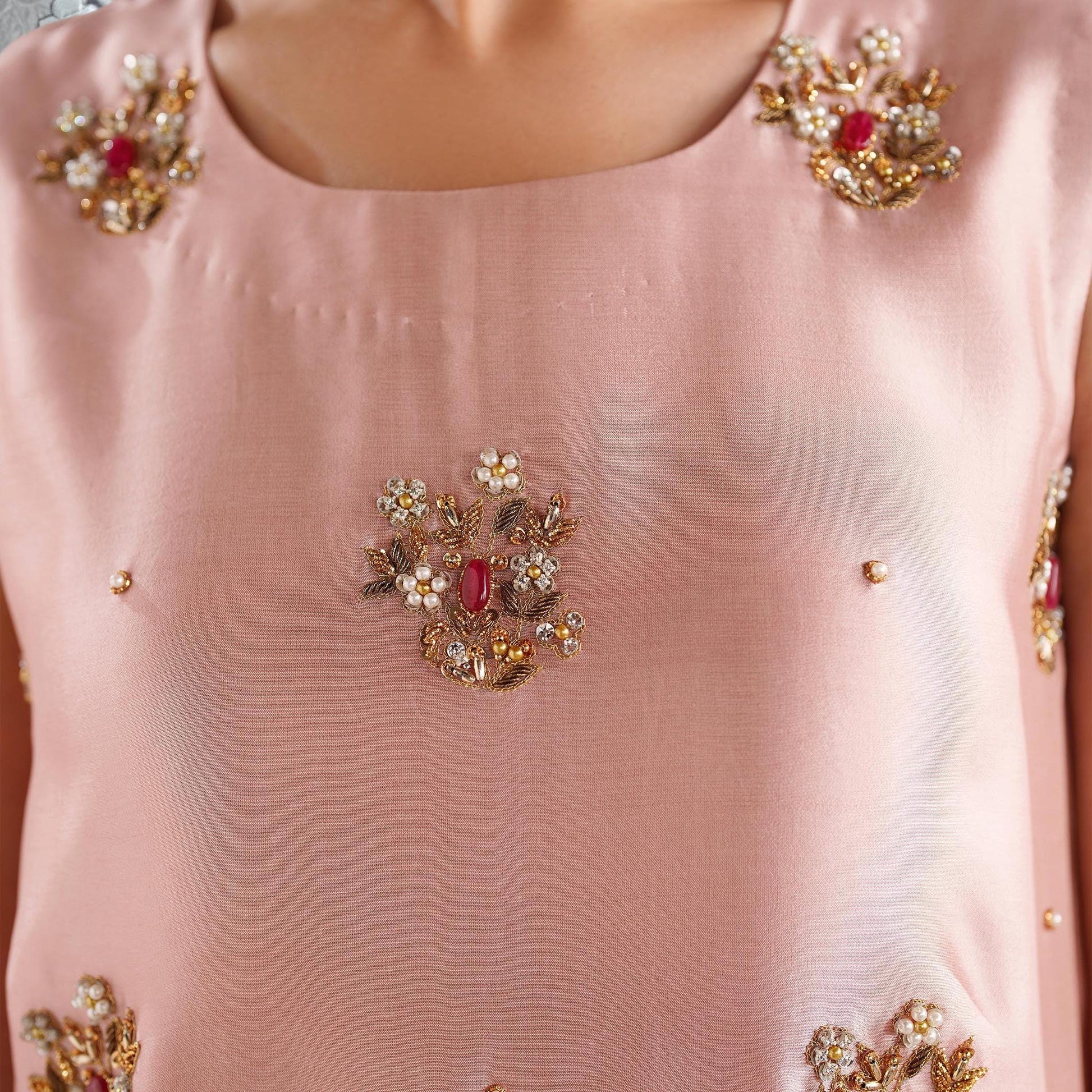 A close-up view of a pink fabric with intricate floral embroidery and gemstones.