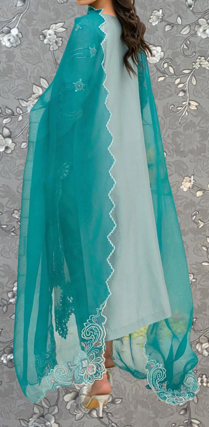 A woman wearing a turquoise and white dress with a matching turquoise shawl, standing against a gray floral background.