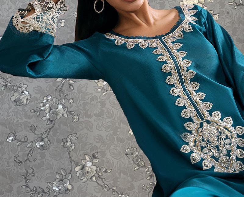 A close-up of a woman wearing a teal dress with intricate embroidery and lace details.
