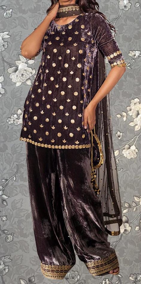 A woman wearing a purple velvet dress with gold polka dots and a matching skirt, standing against a gray floral background.
