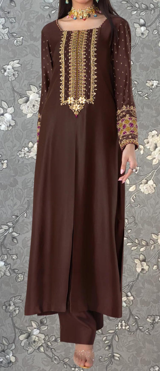 A woman wearing a brown dress with intricate embroidery and gold accents, standing against a gray floral background.