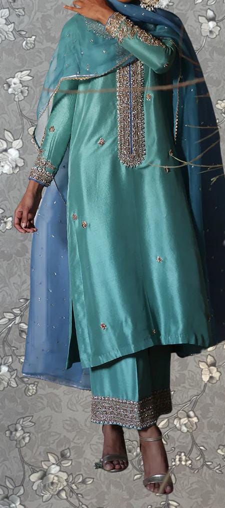 A person wearing a turquoise and blue dress with intricate embroidery and a matching turquoise shawl.