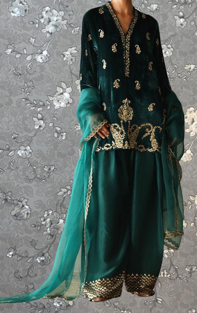 A woman wearing a green velvet dress with gold embroidery and a matching green shawl.